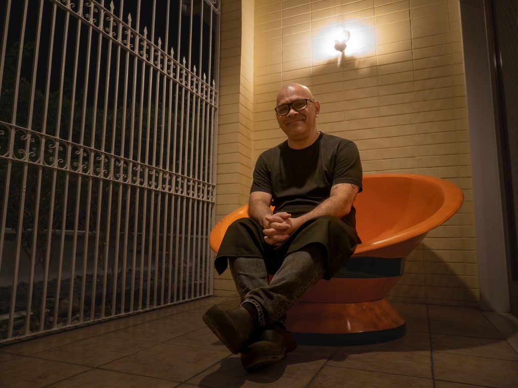 Chef Nats seated on an orange mid-century chair at the entrance of 61 Orange